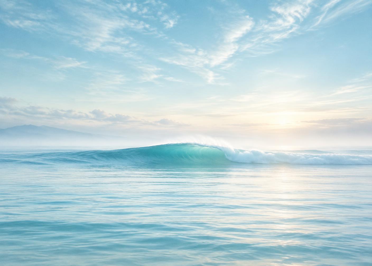 A gentle turquoise wave moving across a calm ocean at dawn